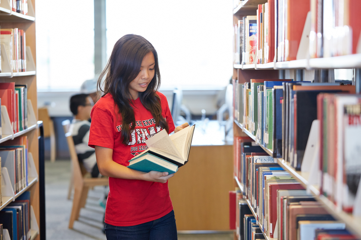 Female student looking at a book in the stacks.